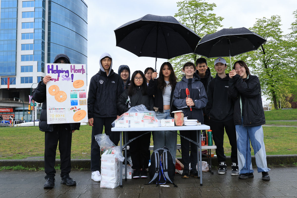 Volunteers under umbrellas handing out care packages at an outdoor table