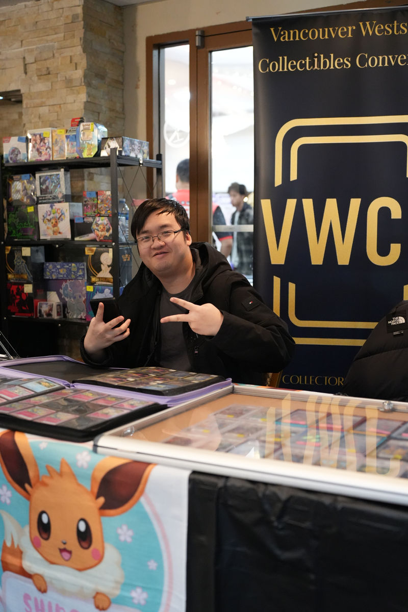 A vendor smiling behind a table of Pokémon cards at the Vancouver Westside Collectibles Convention